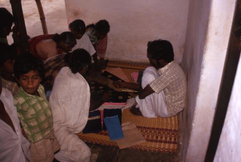 A group of people are looking at spreaded silk clothes (saree, vetti) on a mat