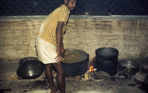 A man cooks in a large pot on a wood stove