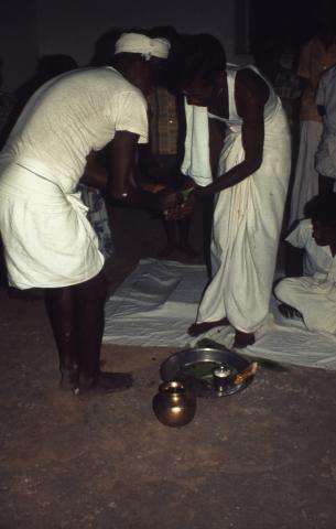 Two men are performing a ritual with betel leaves