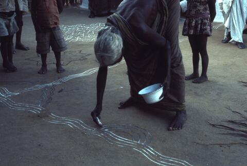 An old woman puts kolam in the soil